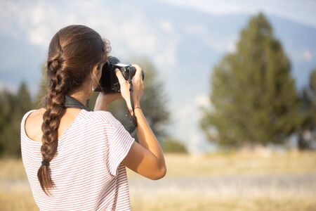Caucasian teenage girl seen from behind taking photos in the forest