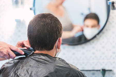 Boy defocuses through the mirror with protective mask while his mother shaves his hair at homeの写真素材