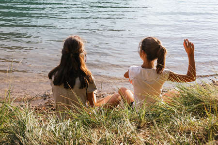 Two sisters sitting trowing stones into the lake in the afternoonの写真素材