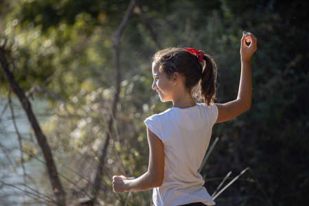 A happy girl trowing a stone with her right hand into the lakeの写真素材