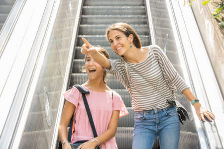 Smiling girls pointing to a landmark outdoors from the escalator
