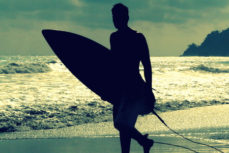 Silhouette of surfer with a board on a sunset evening in Manuel Antonio's National Park main beach,...