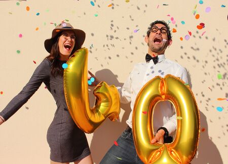 Cheerful couple celebrates a forty years birthday with big golden balloons and colorful little pieces of paper in the air.の写真素材
