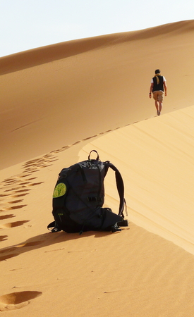 Detail of bag and hiker climbing to the top of the Great Sand Dune in the red dune sea of Erg Chebbi, Morocco.の写真素材