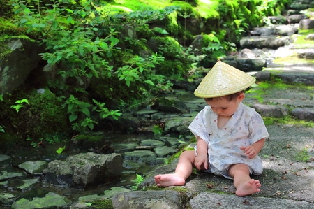 Little baby wearing a traditional yukata custom plays with forest leaves while sitting over the stone steps of Jojakko-ji temple`s main entrance stairs, Kyoto.の写真素材