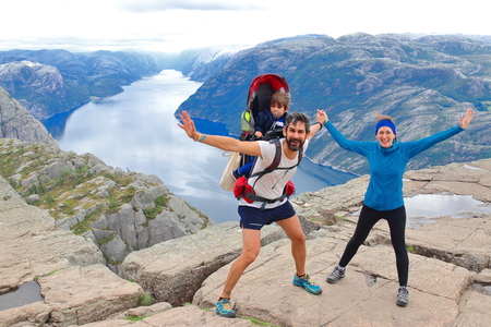 A cheerful couple and their little kid in the summit of the Pulpit Rock (Preikestolen), one of the world's most spectacular viewing points. A plateau that rises 604 meters above the Lysefjord, Norway.の写真素材