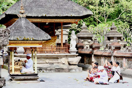 Tirta Empul temple, Tampaksiring, Bali - August 8th of 2019: A full family of locals perform a prying ritual in the main area of this hinduism temple founded around a large water spring in 962 A.D.のeditorial素材
