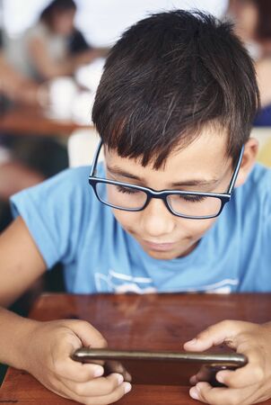 Green eyes boy with glasses playing with his phoneの写真素材