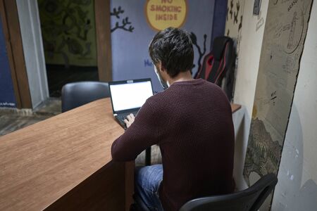 Young man with beard working with his lap top in a desk of a hostelの写真素材