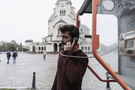 Young man making a a call in a telephone booth