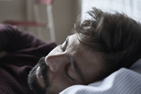 Handsome man sleeping in his bedroom. Man sleeping with alarm clock in foreground. Serene latin man sleeping peacefully.の写真素材