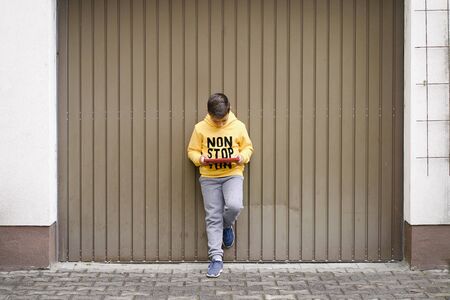 Boy with yellow sweatshirt surfing with his tablet in the street
