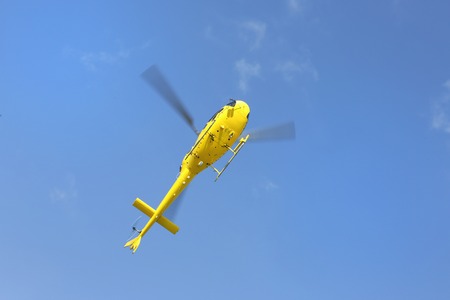 Helicopter rescue, Yellow helicopter in the air while flying on blue sky, bottom view.の写真素材