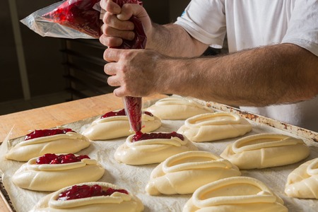 Raw sweet yeast dough on a baking sheet, filling buns jam. Preparation for baking. The concept of chefs and baking.の写真素材