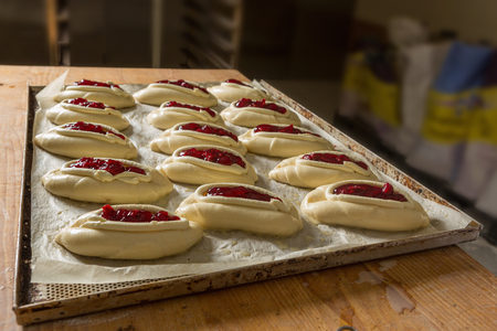 Raw sweet yeast dough on a baking sheet, filling buns jam. Preparation for baking. The concept of chefs and baking.の写真素材