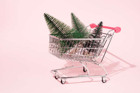 Shopping cart full with Christmas trees on pastel pink background .Minimal New Year or Christmas party concept.の写真素材