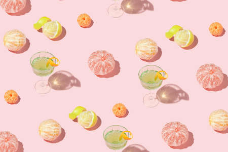 Creative pattern made of exotic cocktail in crystal glass and citrus fruits on pink background....