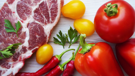 A piece of raw meat and fresh vegetables on a wooden background.の写真素材