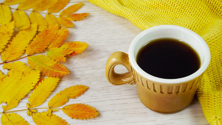 A cup of coffee and colorful autumn leaves on a yellow background.