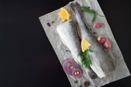 Fresh sea fish with herbs, spices and lemon on a black background.