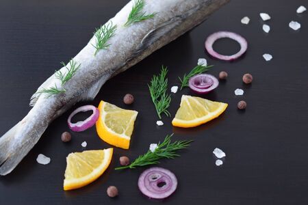Fresh sea fish with herbs, spices and lemon on a black background.