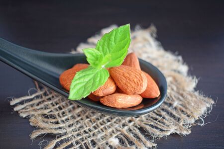 Delicious and healthy almonds. Nuts and a sprig of mint in a spoon on a black background. Healthy diet.の写真素材