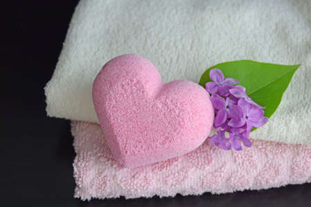 Bath salt in the shape of a heart with a light fragrance of lilac. Soft towels and a flower on a black background.の写真素材