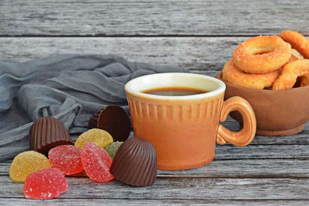 A cup of fresh aromatic tea, chocolates and marmalade on a wooden background.Round cookies in a clay plate.の写真素材