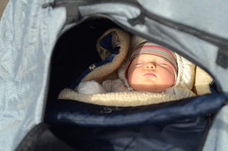 Baby sleeping soundly in a warm stroller on a sunny winter dayの写真素材