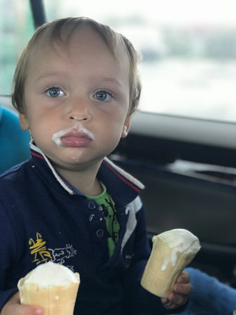 Little boy eats 2 ice cream while sitting in a car seat. Children safety in a car concept. Child...
