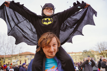 Halloween. Little boy dressed as Batman sits on his dads neck. Colorful confetti swirls in the airの写真素材
