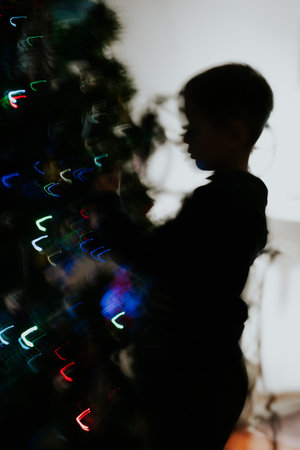 Merry Christmas and Happy New Year. Preschooler near Christmas tree decorated with burning colorful garlandの写真素材
