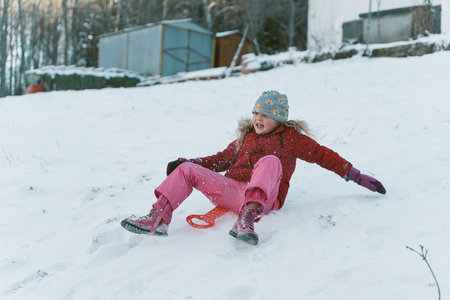 Little girl in warm clothes is sledding down a hillの写真素材