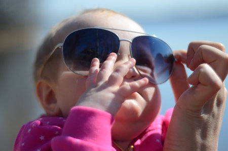 Little girl in big sunglasses. Mom's hand helps to keep the glasses on her faceの写真素材