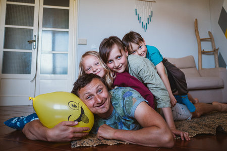 Happy father and his three children are lying down on the floor making time for family funの写真素材