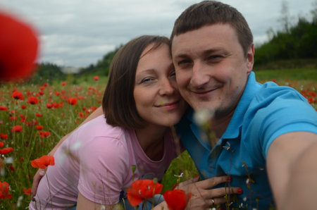 Young couple in love in a field among blooming red poppiesの写真素材