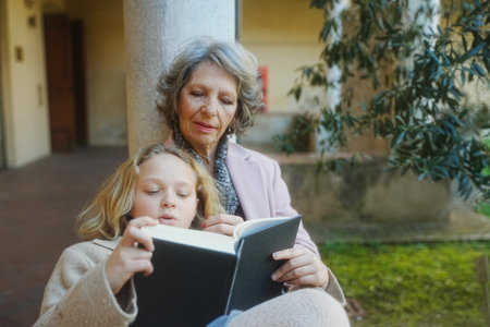 Spring. Grandmother and granddaughter reading a book in the library yardの写真素材