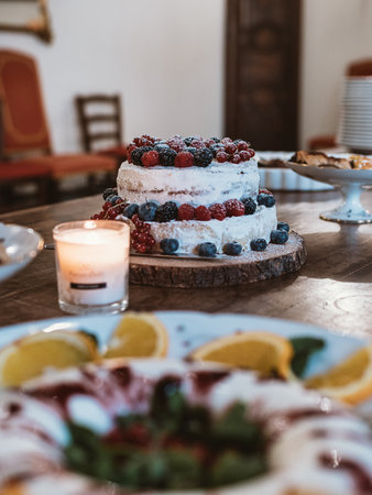 Burning candles and home-made cake decorated with fresh berries on wooden table set for party. Birthday party celebrationの写真素材