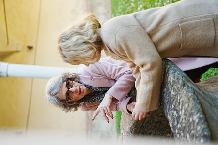 Elderly woman talks to a young girl outdoors, both wearing coats. The interaction appears warm and engaging, highlighting a generational connection amid a serene settingの写真素材