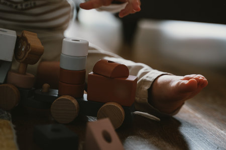 Child engrossed in play with a wooden toy train, bare feet visible. Focused activity on a hardwood floor, highlighting early childhood development and creativity through playの写真素材