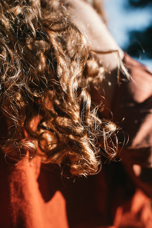 Close-up image of curly hair shining in natural sunlight, partially covering a person's face. The focus is on texture and light, highlighting the rich details of the curlsの写真素材