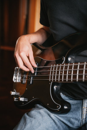 Close-up of a musician's hand playing a bass guitar, showing the detail of finger placement and...