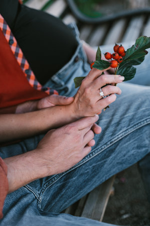 Close-up of hands holding vibrant red hawthorn berries, emphasized connection and tenderness. Rings sparkle, jeans and plaid shirt create a casual, intimate settingの写真素材