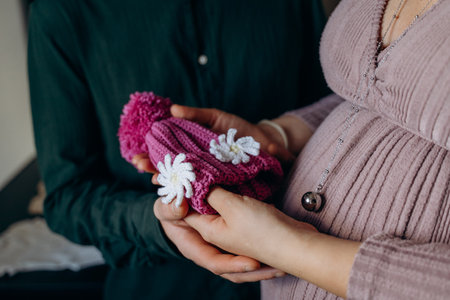 Pregnant couple tenderly holding a pair of small baby booties with delicate floral decoration. Symbolizes anticipation and excitement for their upcoming newborn arrivalの写真素材