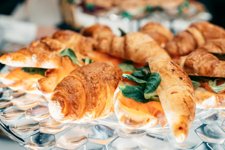 Freshly baked croissants filled with flavorful smoked salmon and crisp greens, arranged on a clear glass plate, highlighting texture and enhancing visual appeal for culinary presentationの写真素材