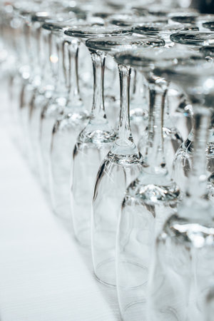 Transparent wine glasses are arranged upside-down in a neat row on a smooth white surface. Each...