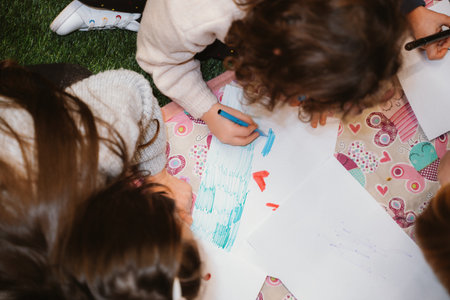 Children gathered on the floor engaging in creative drawing. Focused expressions as they use vibrant colors on paper. Collaborative atmosphere fosters creativity and learningの写真素材