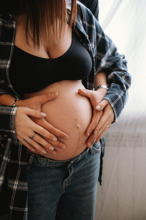 Close-up of a pregnant woman with hands gently resting on her belly, symbolizing support and love. Captures a moment of anticipation and togetherness in parenthoodの写真素材