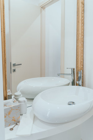 The real estate photo highlight mirror of a stylish bathroom vanity featuring a large rectangular mirror with a golden wooden frame, a white sink with a minimalist faucet and a white countertopの写真素材