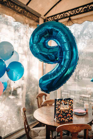 Blue number 9 balloon at a festive birthday party setting. Helium balloons decorate the scene...